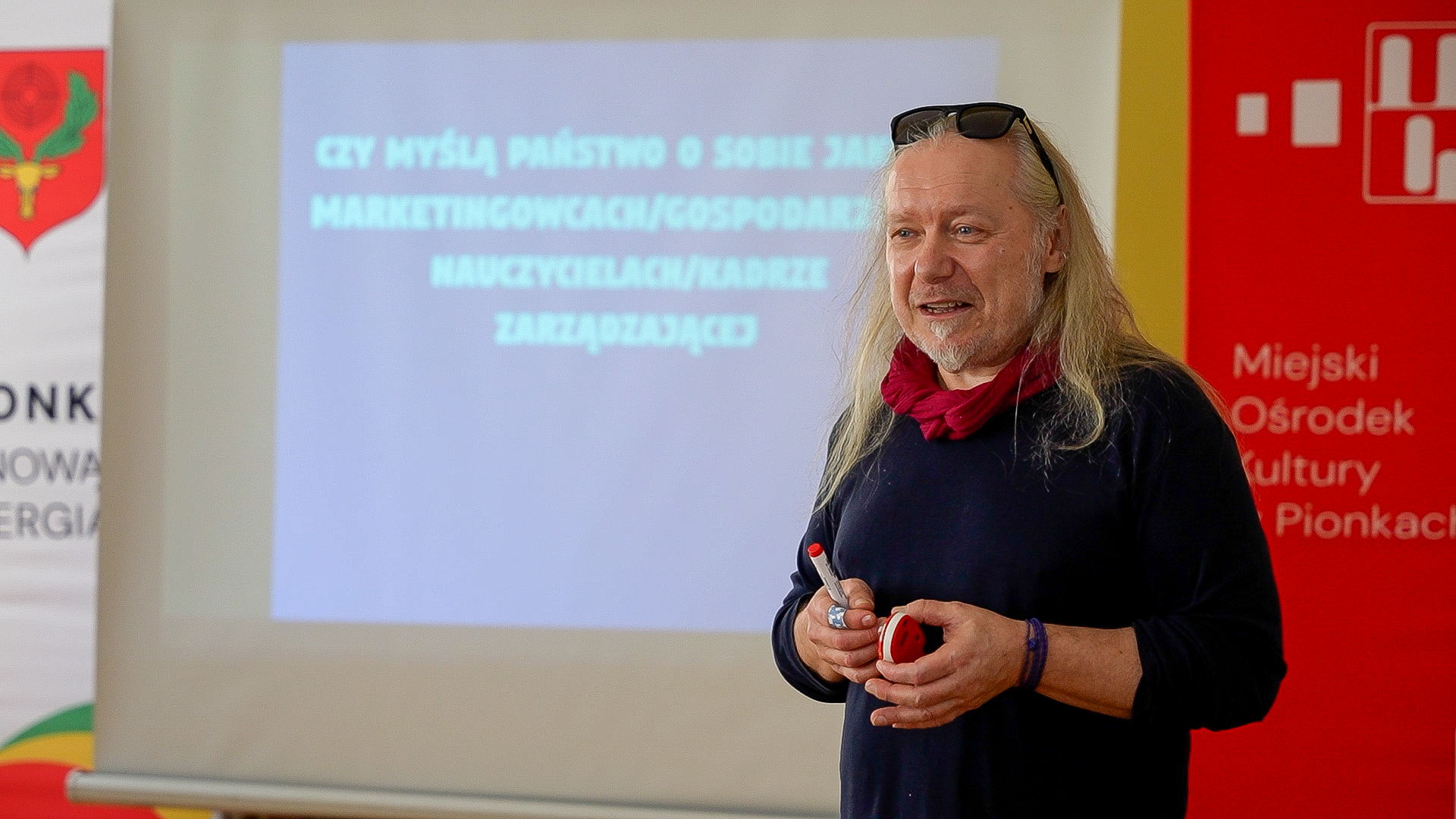 Mężczyzna, siwe włosy do ramion, około 55-60 lat; kobieta brunetka w okularach,  w upiętych włosach